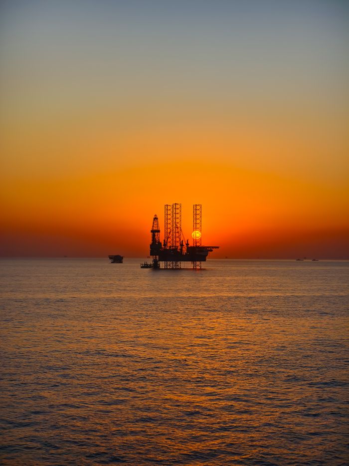 Silhouette of an oil rig against a vibrant sunset over the ocean, capturing the essence of industrial beauty.