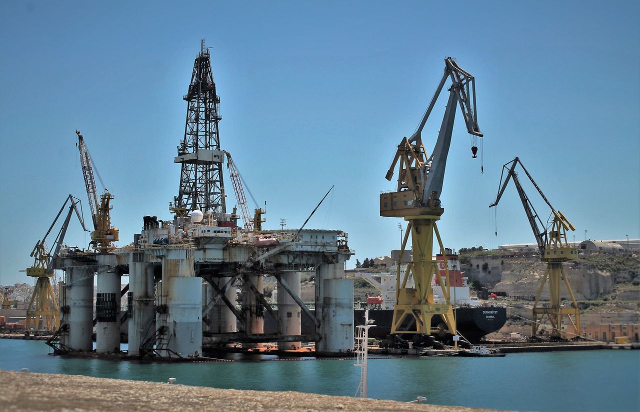Various modern construction cranes located near harbor during shipbuilding against cloudless blue sky